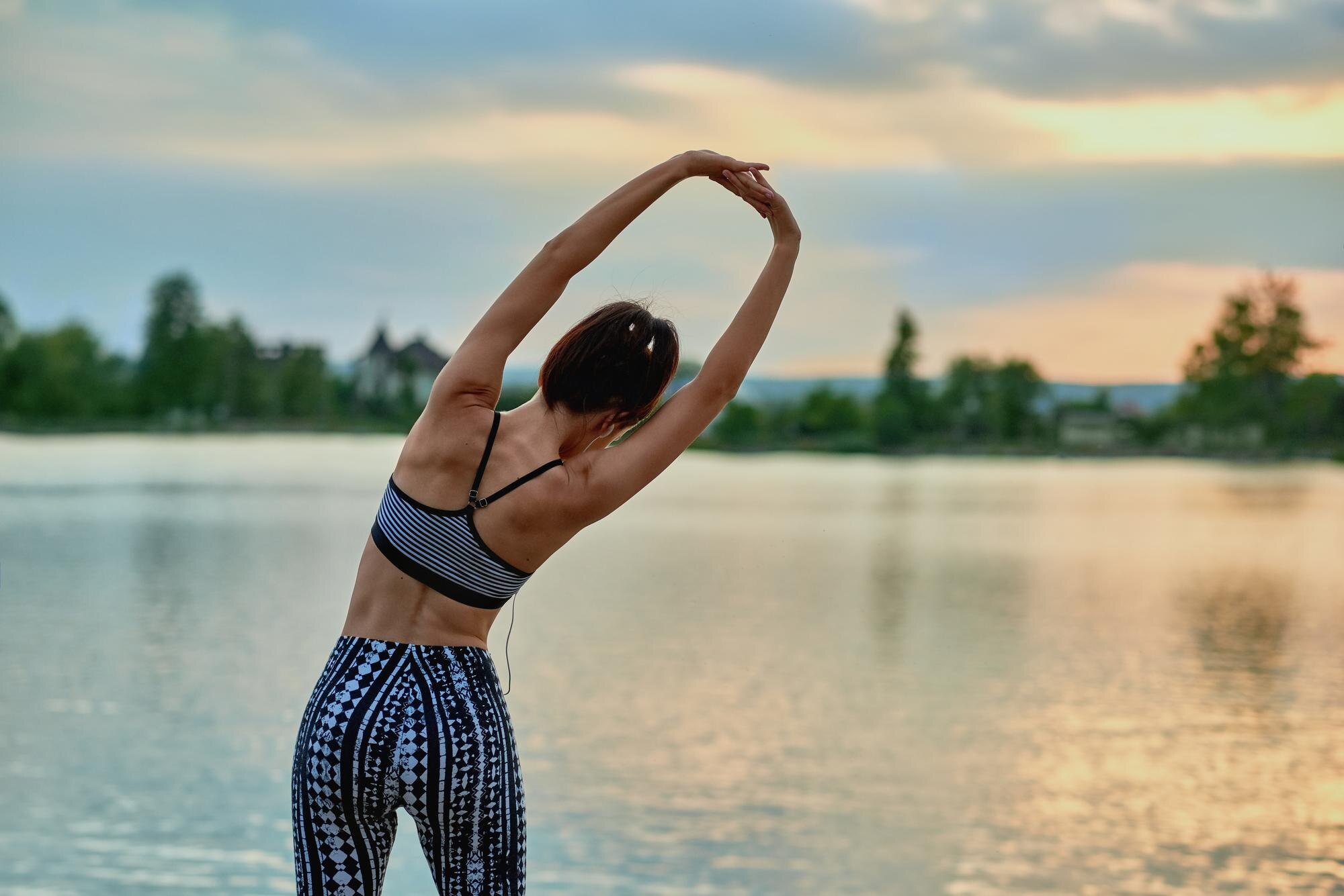 Person stretching gently outdoors near a lake